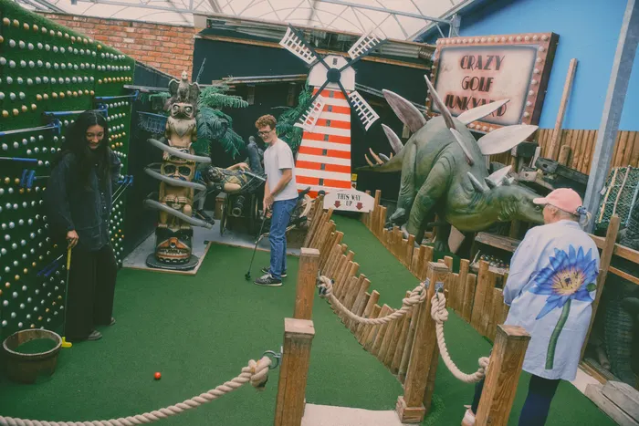 Players on Hole 6 of the Crazy Golf Junkyard at the Flower Bowl, with the windmill, totem pole and stegosaurus