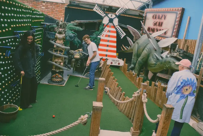 Players on Hole 6 of the Crazy Golf Junkyard, with the windmill and stegosaurus